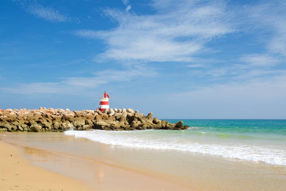 A beach with a rocky breakwater and a lighthouse.