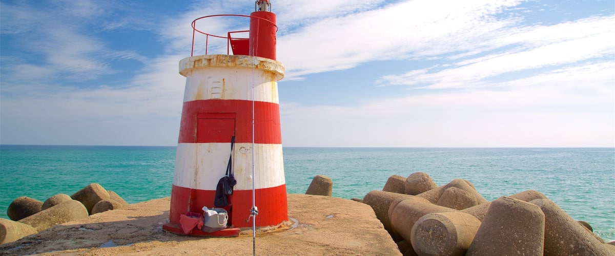 A red and white lighthouse on a rocky shore with turquoise water.