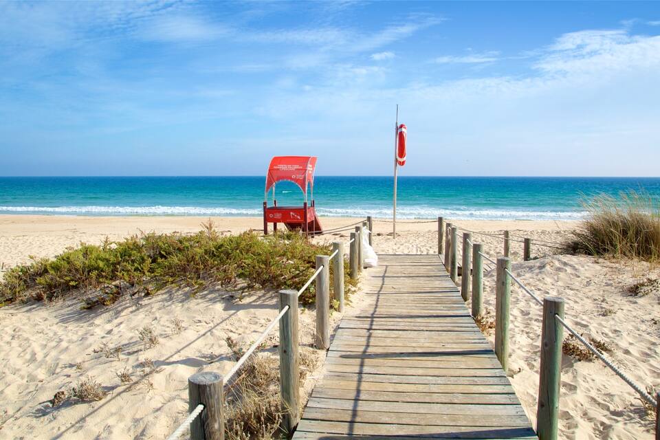 A wooden boardwalk leading to a lifeguard chair on a sandy beach with the ocean in the background.
