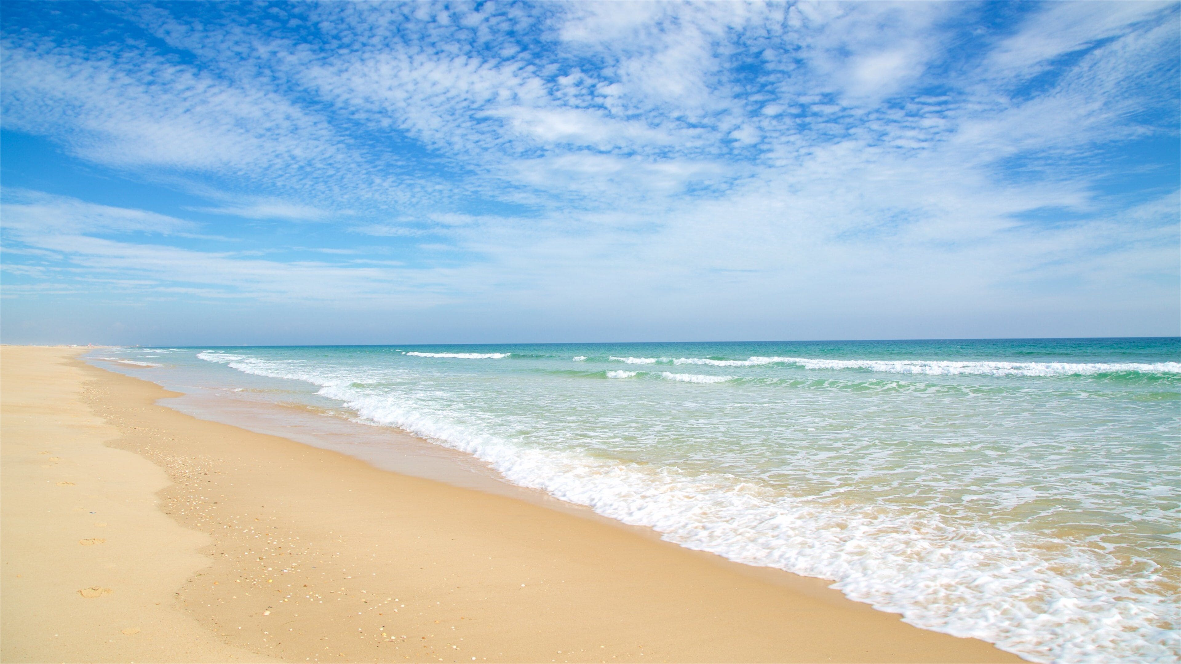 A sandy beach with gentle waves and a clear blue sky.