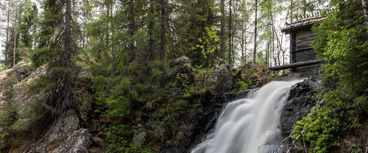 A waterfall cascading over rocks in a forested area with a wooden structure nearby.