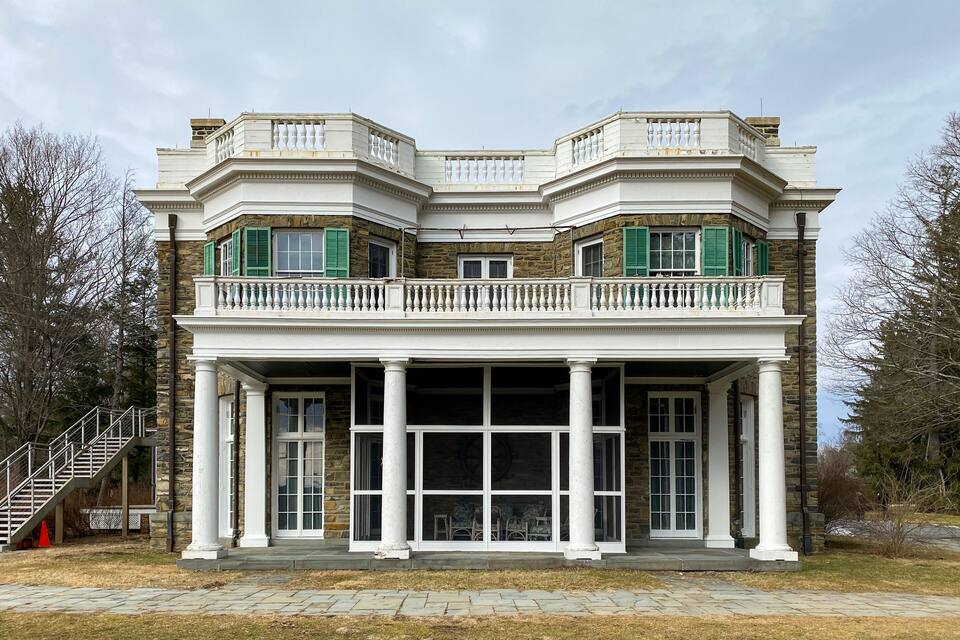 A large, stately building with a symmetrical facade, stone detailing, and green shutters.