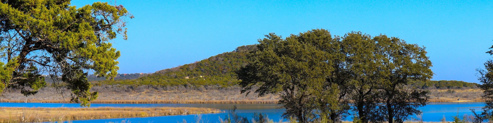 Stillhouse Hollow Lake landscape with trees, and a lush meadow at Dana Peak Park, Harker Heights Texas