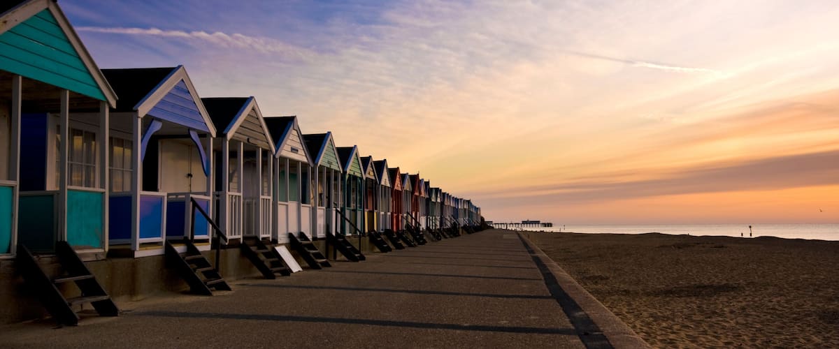 A row of colorful beach huts along a seaside promenade during sunset.