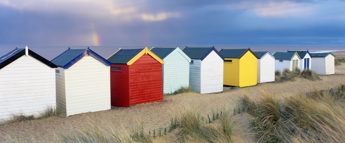 A row of colorful beach huts along a sandy beach with dunes and a stormy sky.