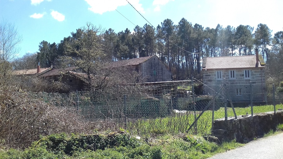 Paisagem rural com casas de pedra, cerca de arame e muro de pedra.