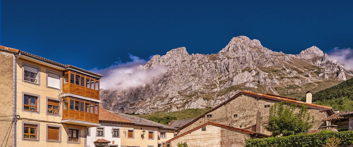 A mountain with rocky peaks and a village with traditional buildings.