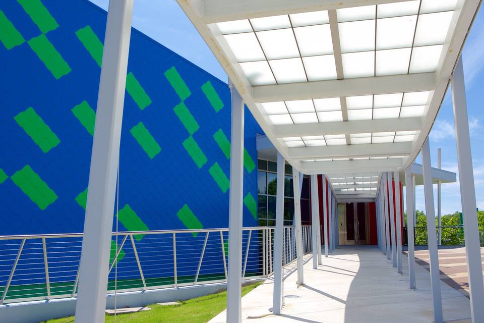 A modern building with a blue facade and green diamond patterns, a covered walkway with white columns, and a clear sky.