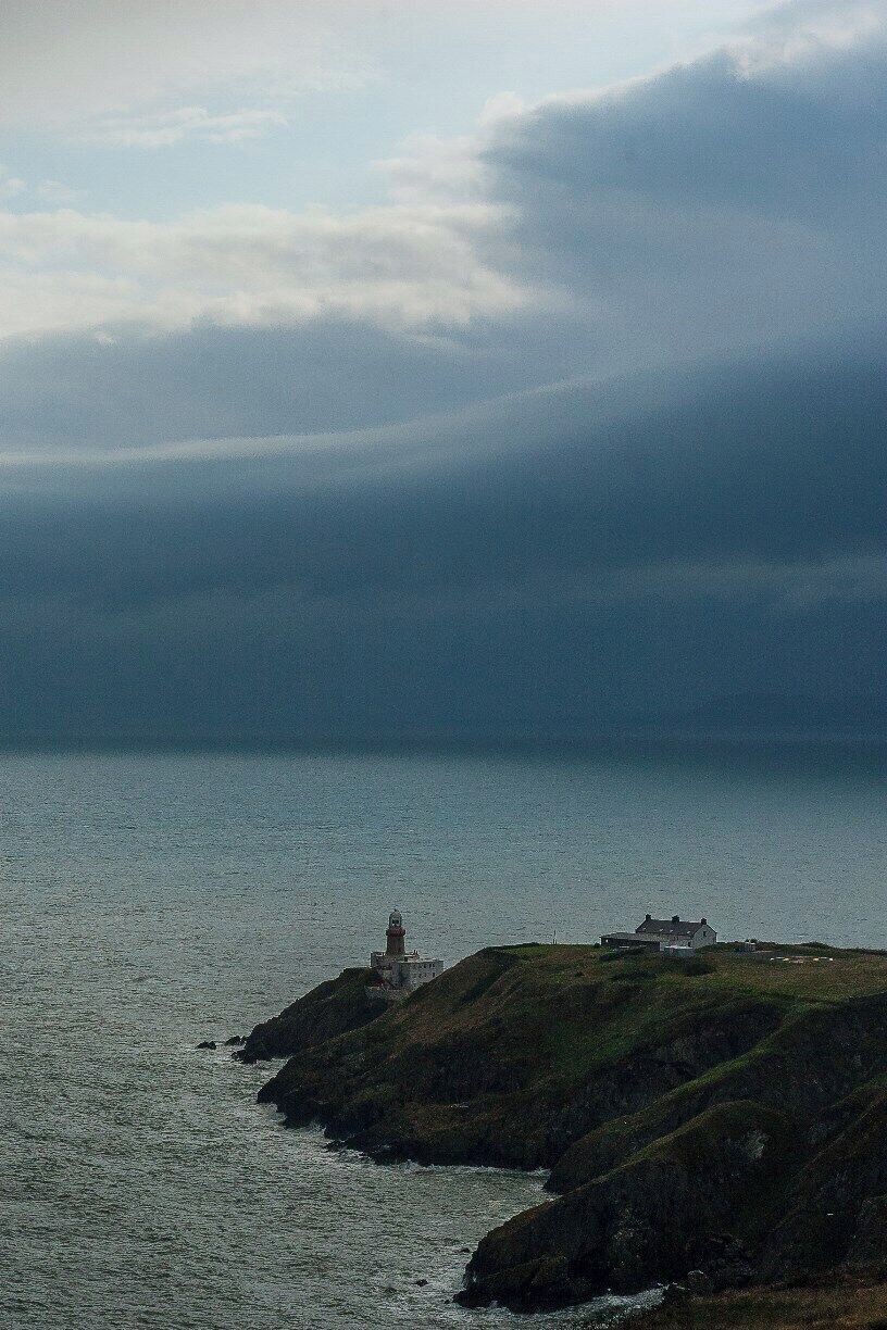Un faro sobre una costa rocosa, con una casa al fondo.