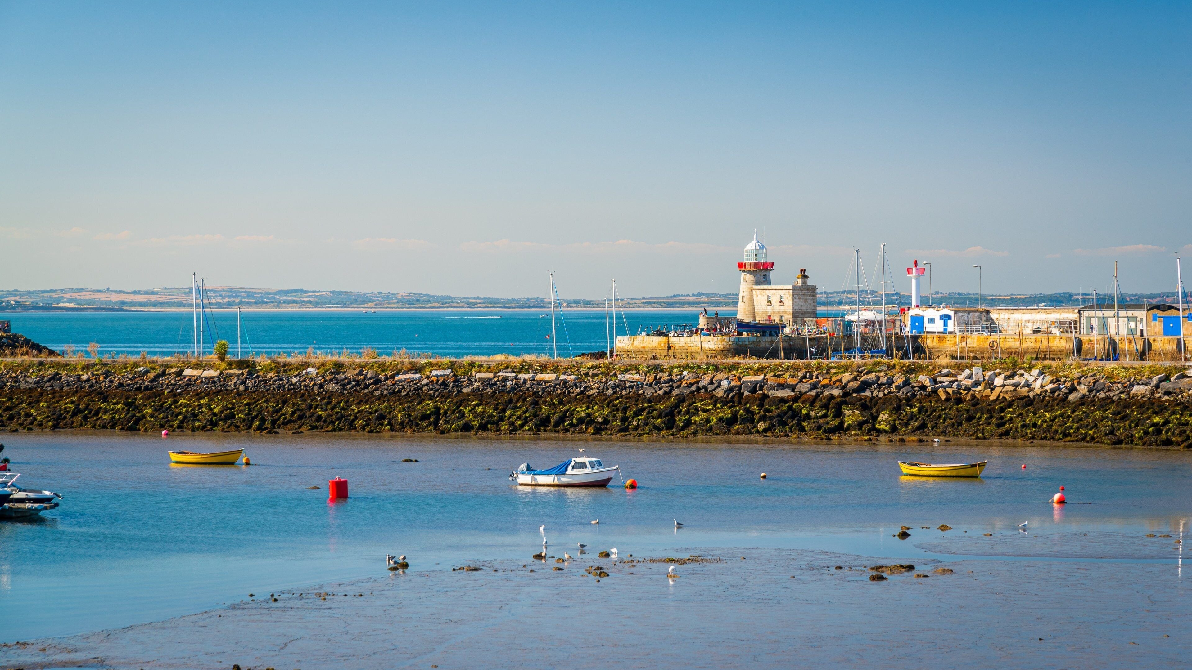 A coastal scene with a lighthouse, boats, and a rocky shoreline.