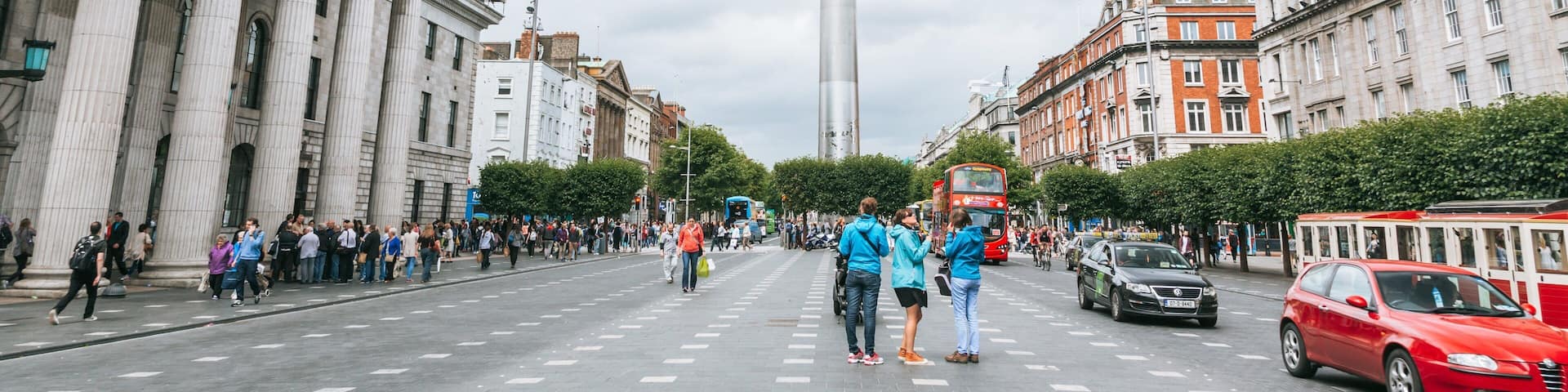 A busy city street with classical architecture, a tall monument, and a red double-decker bus.