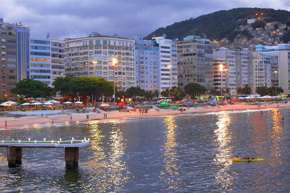 Eine Küstenstadt mit Strand, Wasserspiegelungen und einer Hügelkulisse im Hintergrund.