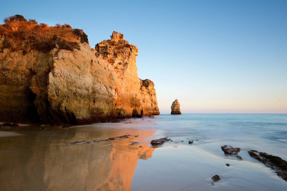 A coastal landscape with a large rock formation and a smaller rock in the water.