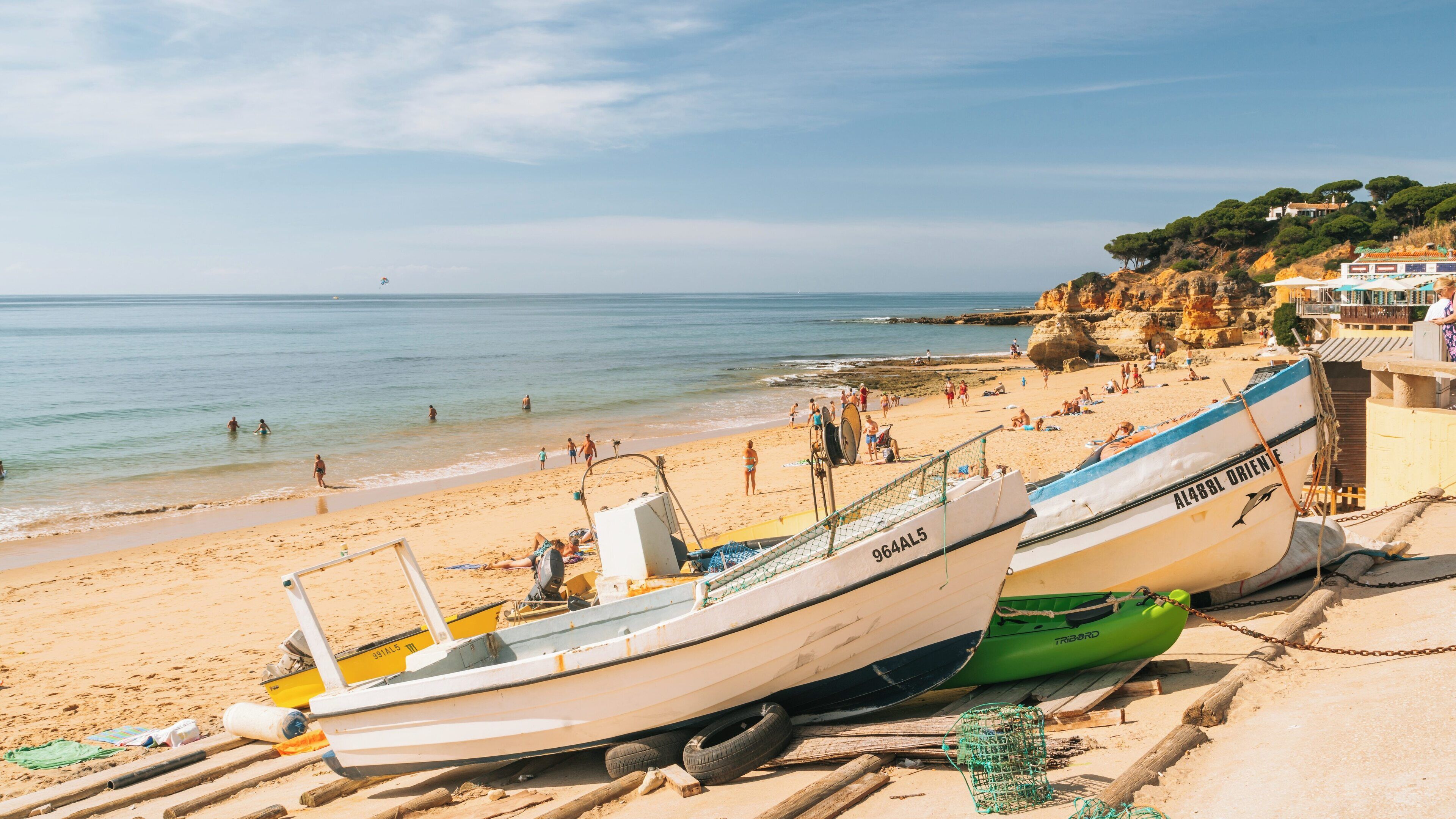 Beautiful Praia dos Olhos de Agua in Albufeira, Portugal features sandy shores, colorful fishing boats, and people enjoying the sunny beach day