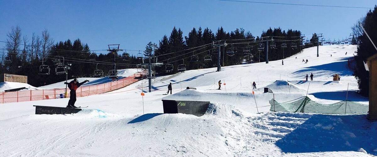 A snowy ski slope with ski lifts, trees, and a clear blue sky.