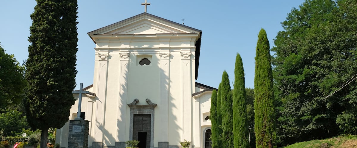 A white church with a cross on top, surrounded by tall cypress trees and a well-maintained lawn.