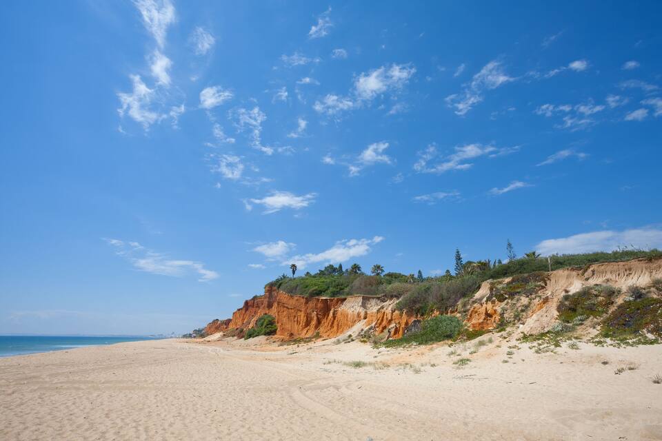 A sandy beach with a clear blue sky and rocky cliffs.