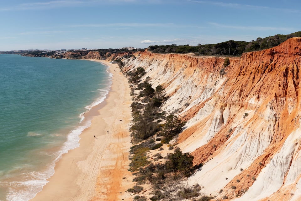 A coastal landscape with a sandy beach and a steep cliff.