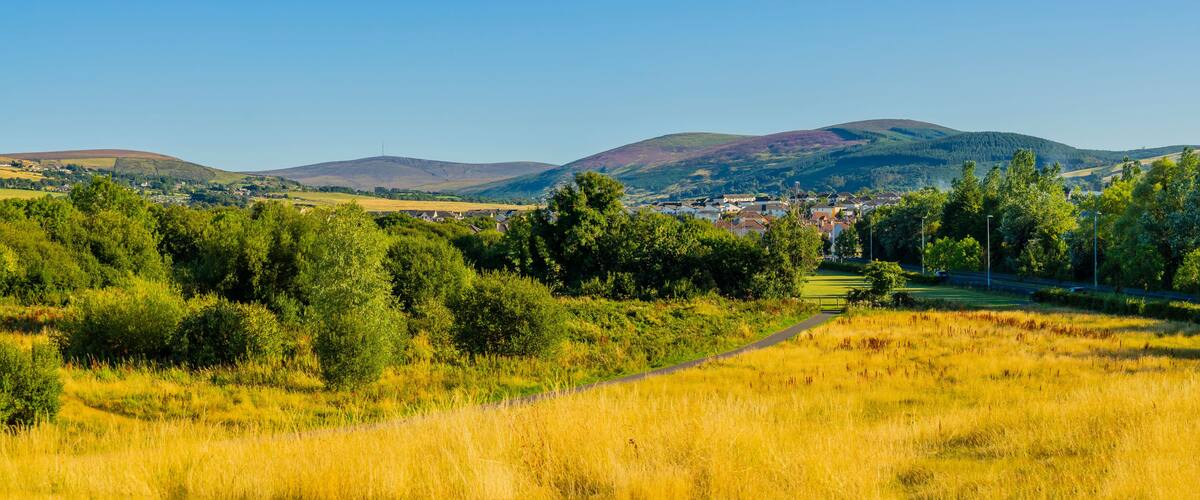 A rural landscape with rolling hills, a village in the distance, and a clear blue sky.