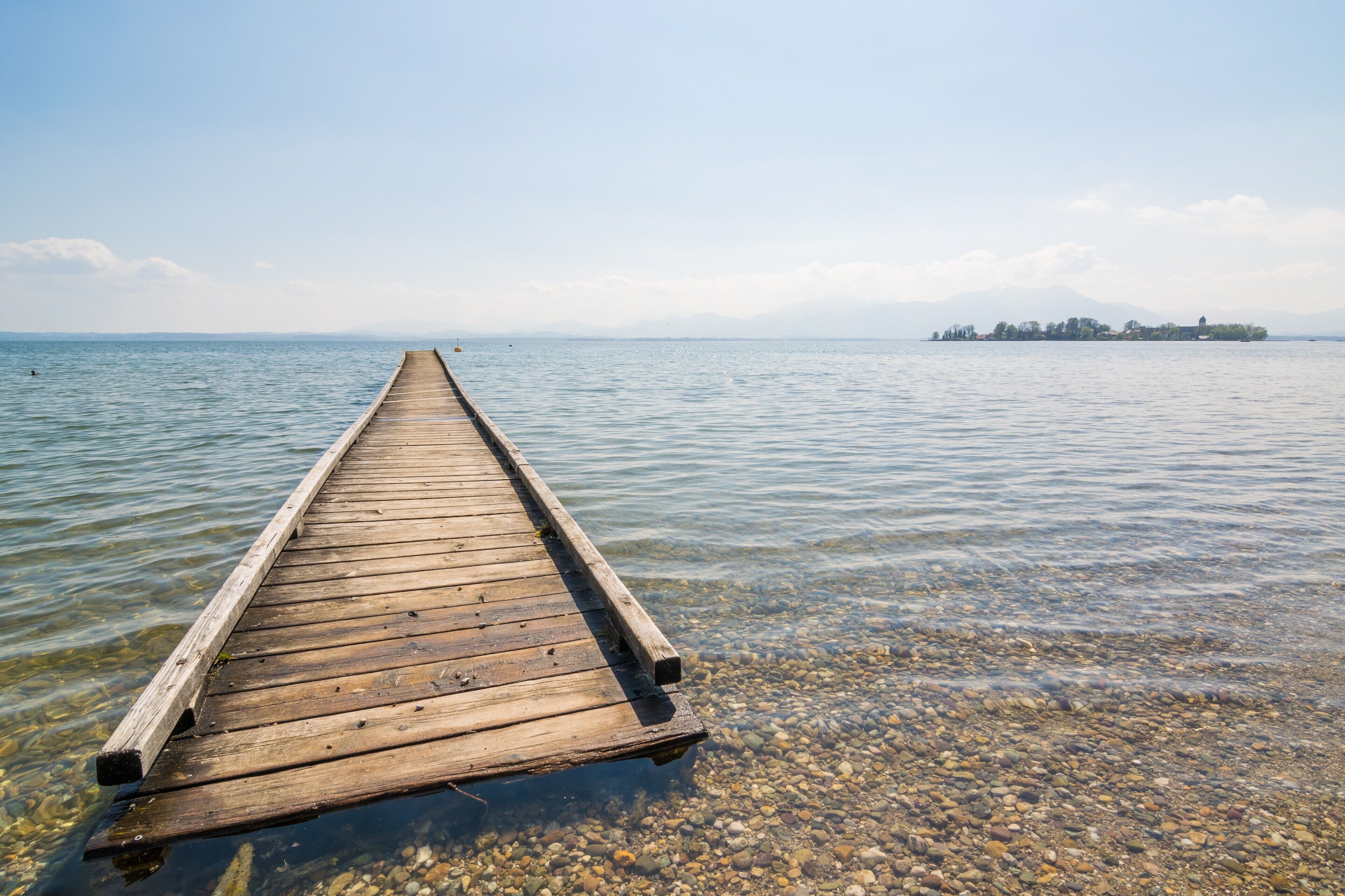 A wooden pier extending into calm waters with a distant island and mountains in the background.