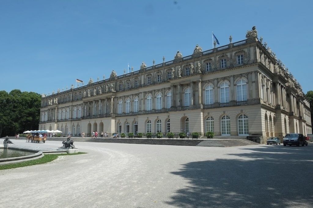 A large, historic building with classical architecture, a fountain, and a clear blue sky.
