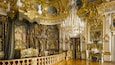 Ein prachtvoller Raum mit aufwändigen Golddekorationen, einem prächtigen Kronleuchter und einem großen Wandgemälde an der Decke.