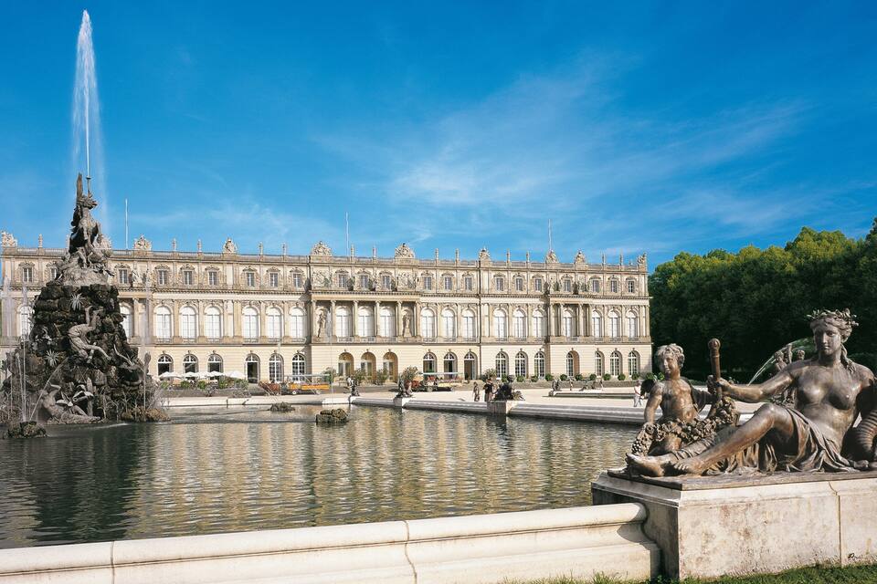 A grand palace with a large fountain and statues in a park.