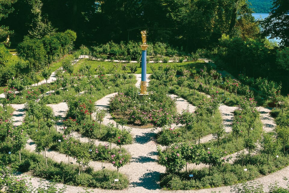 A circular garden with a central statue, surrounded by various plants and trees.