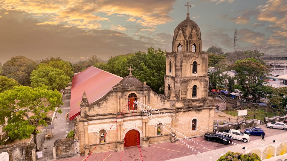 A historic church with a bell tower and a red-roofed building nearby.