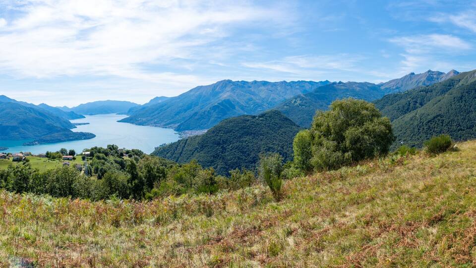 A mountainous landscape with a lake, forested hills, and a small building on a hill.
