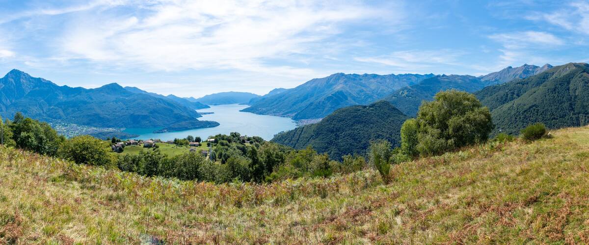 A mountainous landscape with a lake, forested hills, and a small building on a hill.