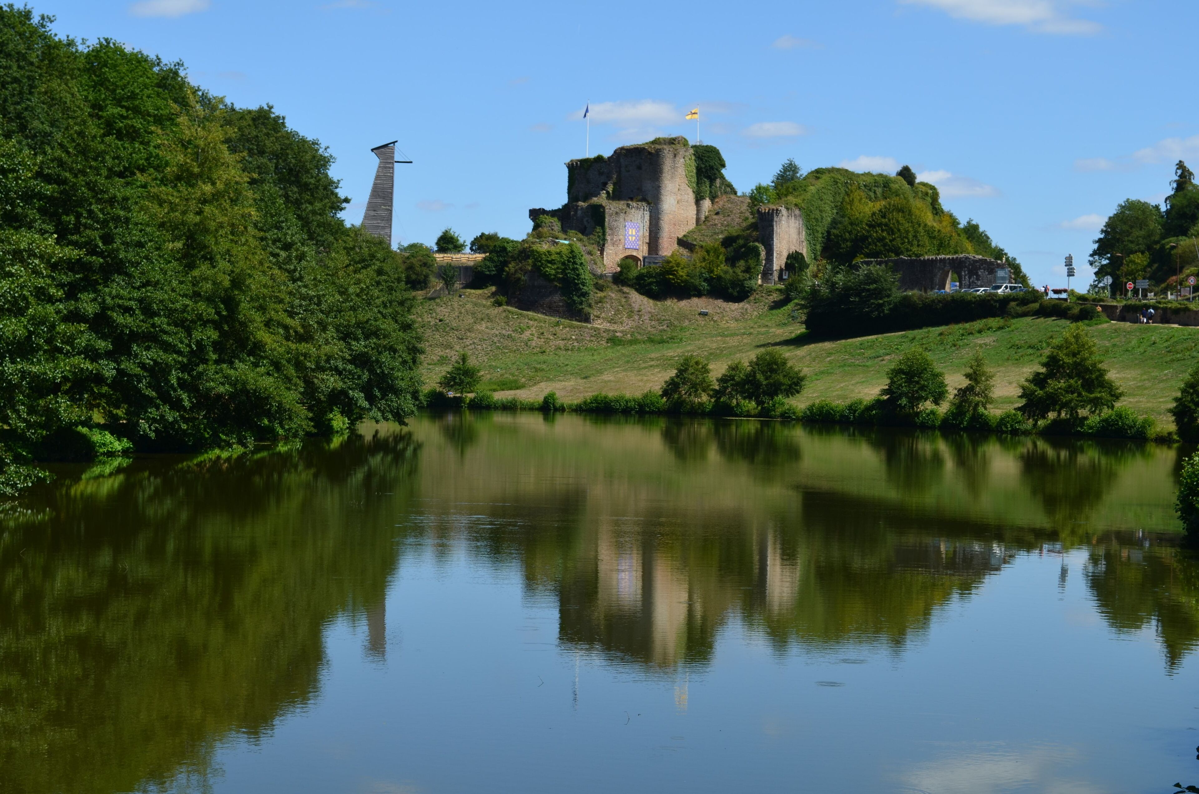 A castle on a hill overlooking a calm river, surrounded by lush greenery.