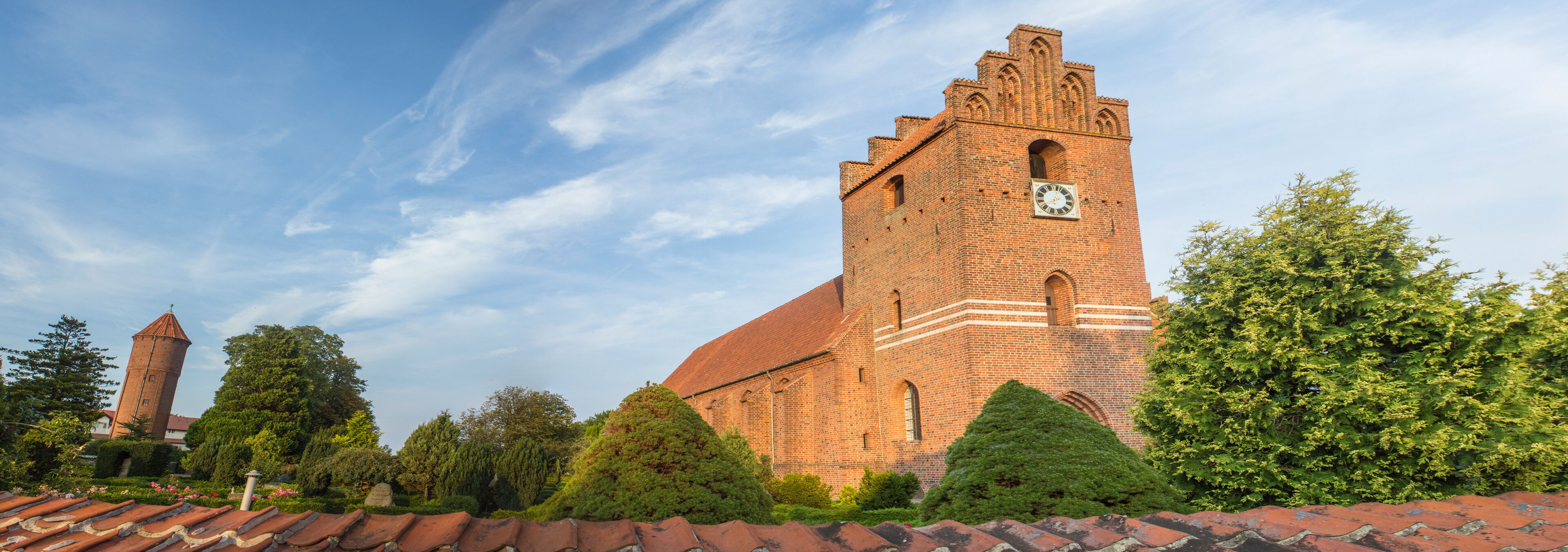 A large brick church with a clock tower and a smaller tower in the background.