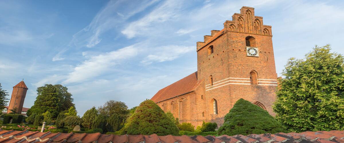 A large brick church with a clock tower and a smaller tower in the background.