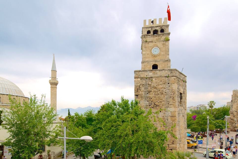 A historic tower with a clock, a mosque with a dome, and lush green trees in the foreground.