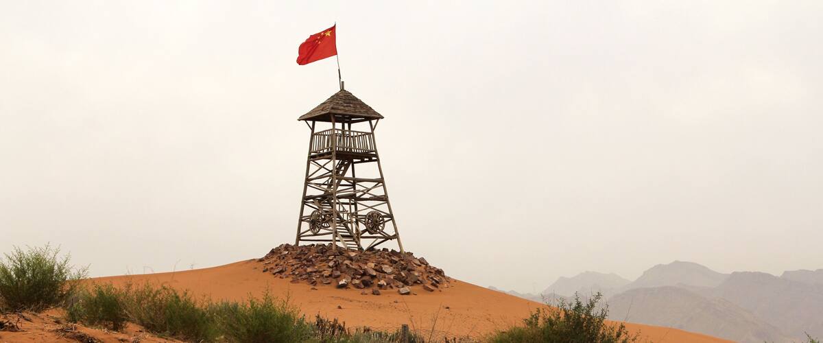 A sand dune with a wooden watchtower and a red flag on top.