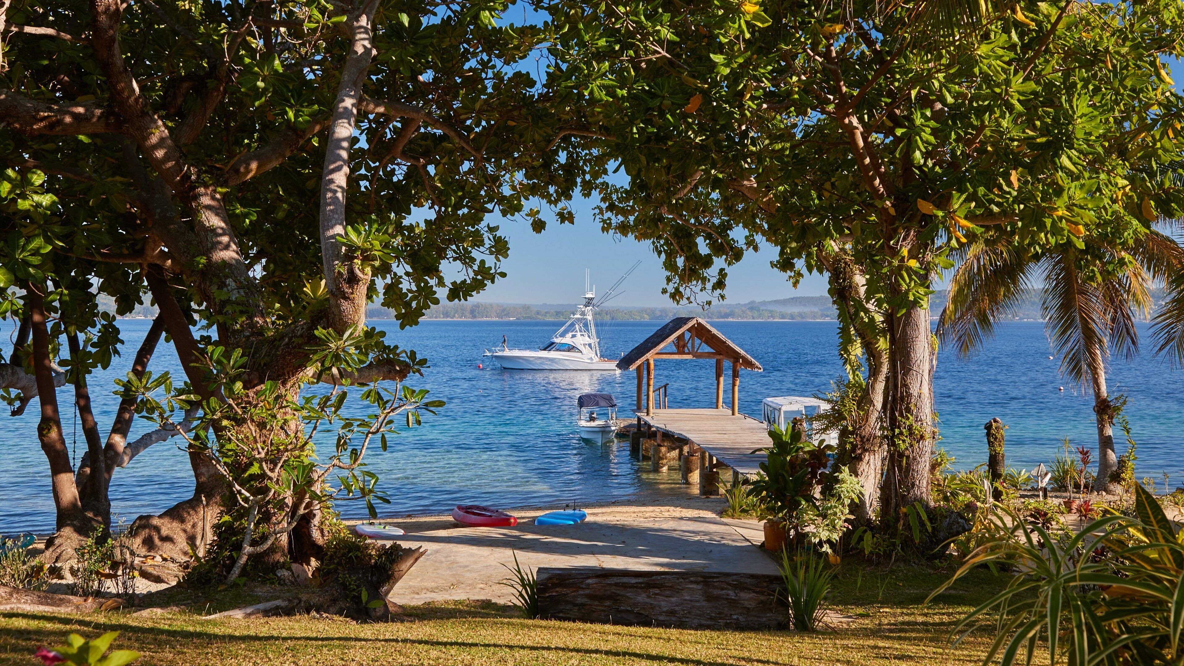 A dock with a small boat, a wooden pier, and a thatched-roof structure by a calm lake.