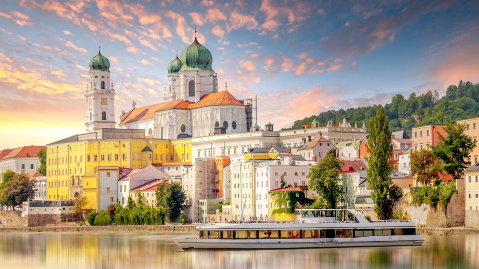 A historic church with two green domes, a river, and a yellow building in the foreground.