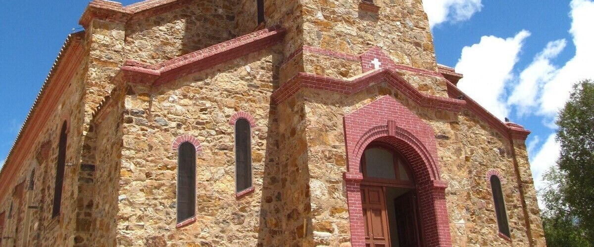 A stone church with a bell tower, arched windows, and a red door.