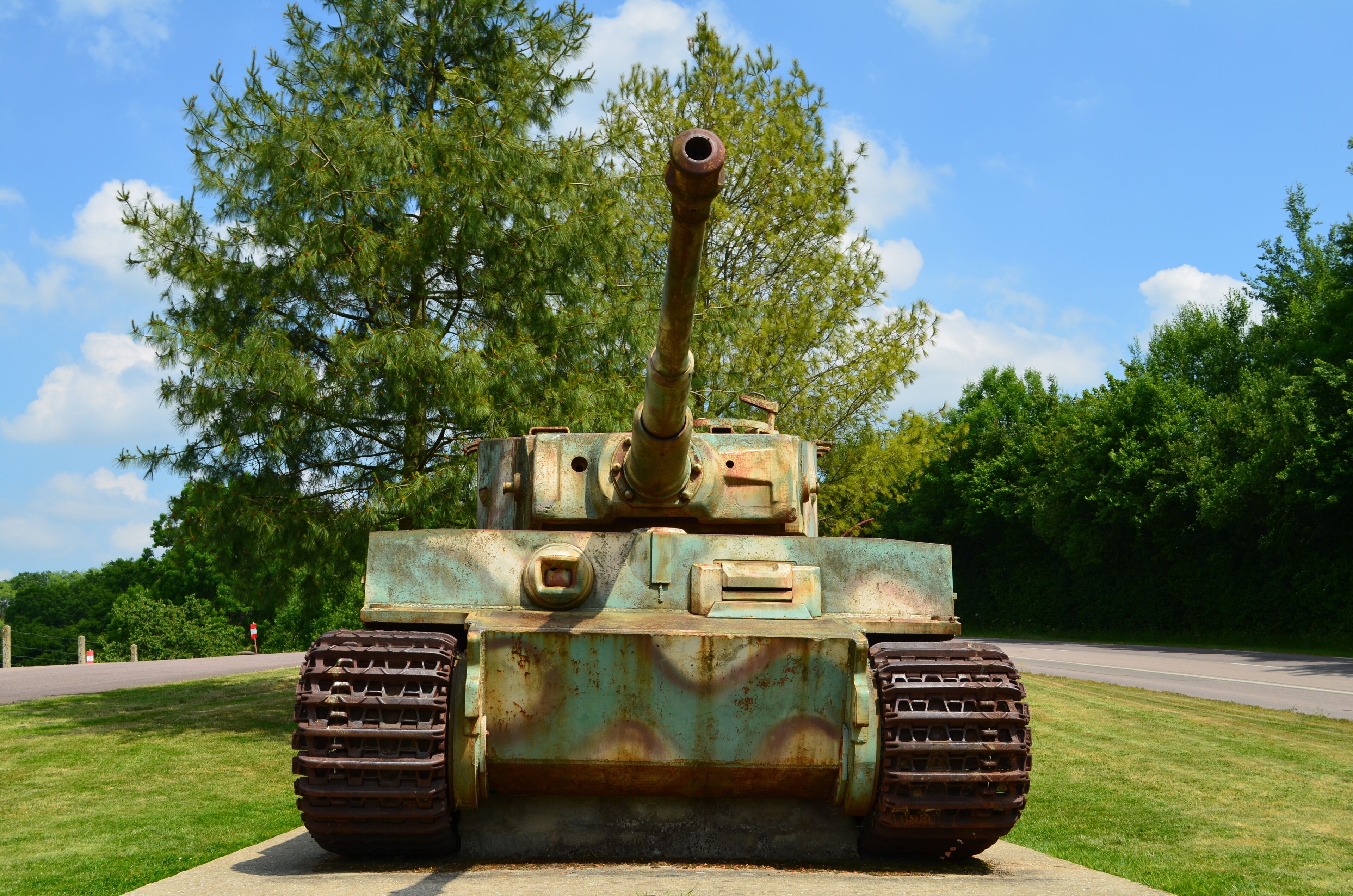 A rusted military tank with a long barrel, positioned on a grassy area with trees in the background.