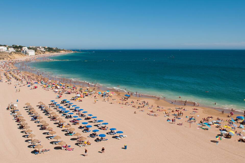 A crowded beach with numerous umbrellas and people enjoying the sunny weather.
