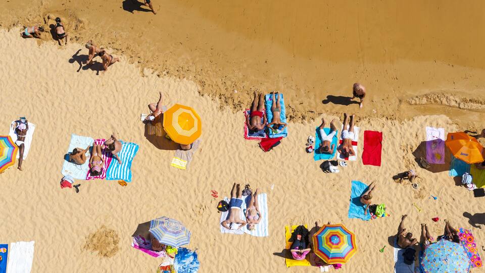 A crowded beach with people sunbathing, umbrellas, and beach towels.