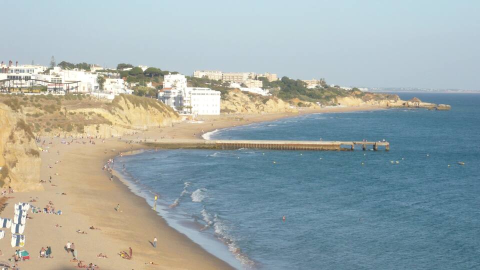A beach with people, a pier, and buildings in the background.