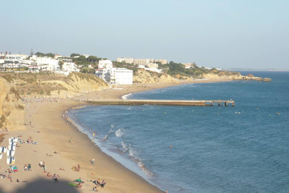 Una playa con gente, un muelle y edificios al fondo.
