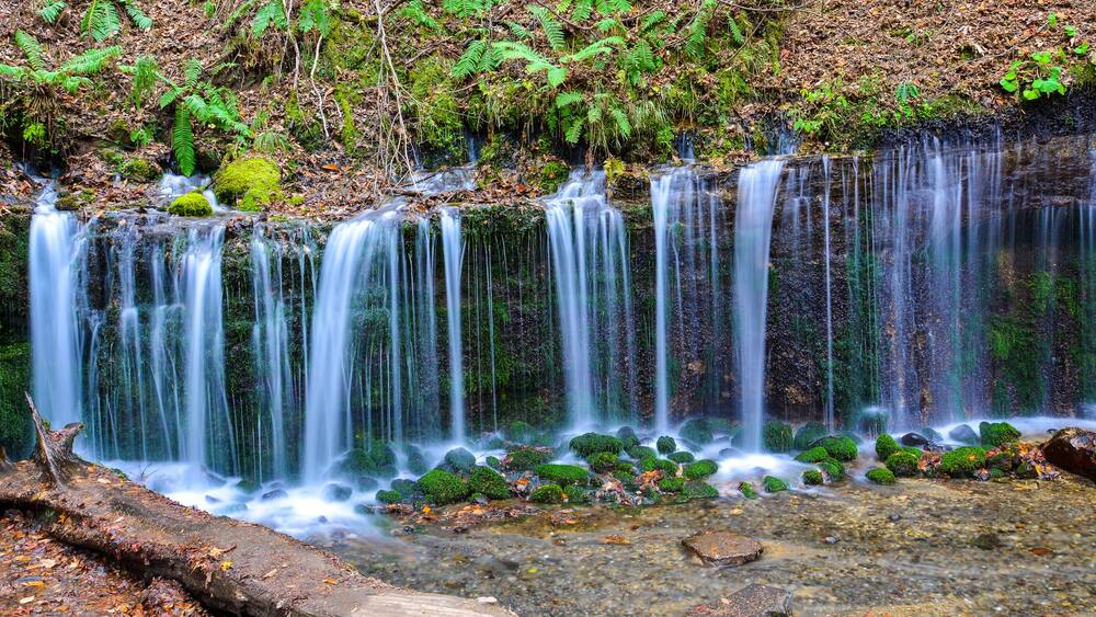 A multi-tiered waterfall with moss-covered rocks and ferns.