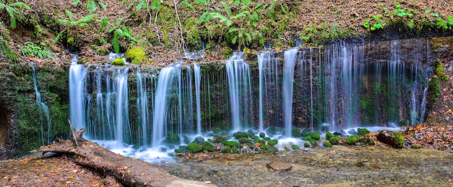 A multi-tiered waterfall with moss-covered rocks and ferns.