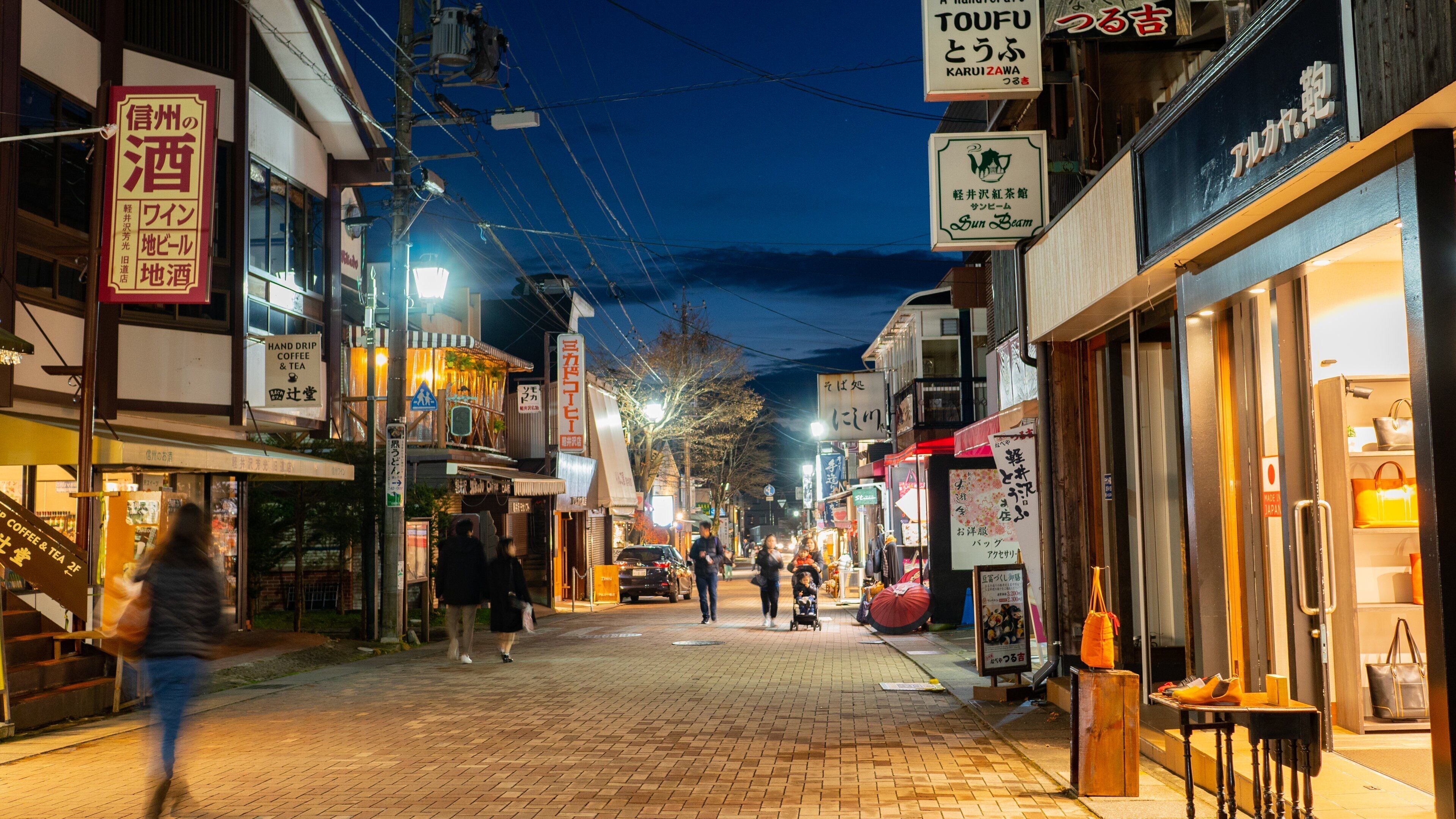 A nighttime street scene with illuminated signs, brick pavement, and pedestrians.