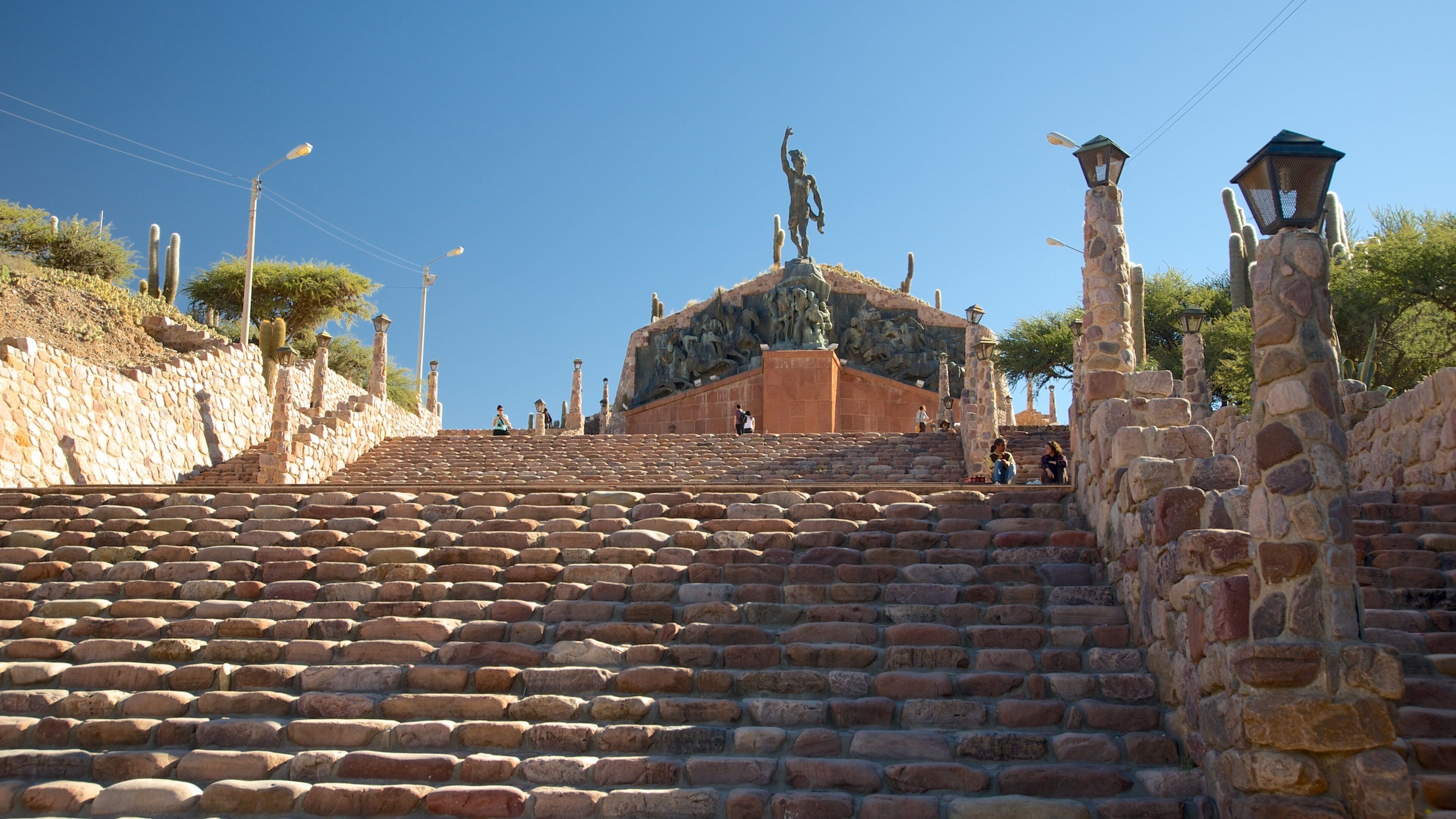 A stone staircase leading up to a historical building with statues and a stone wall with cacti.