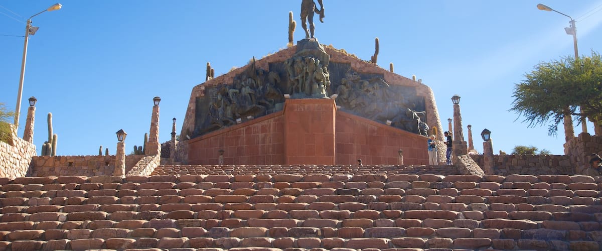 A stone monument with a statue on top, surrounded by stone benches and cactus sculptures.