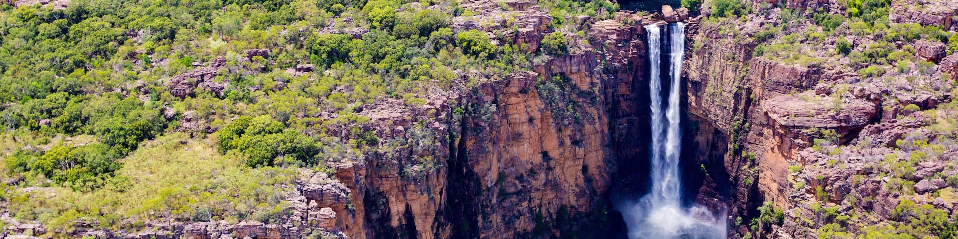 A waterfall cascading down a steep cliff surrounded by green vegetation.